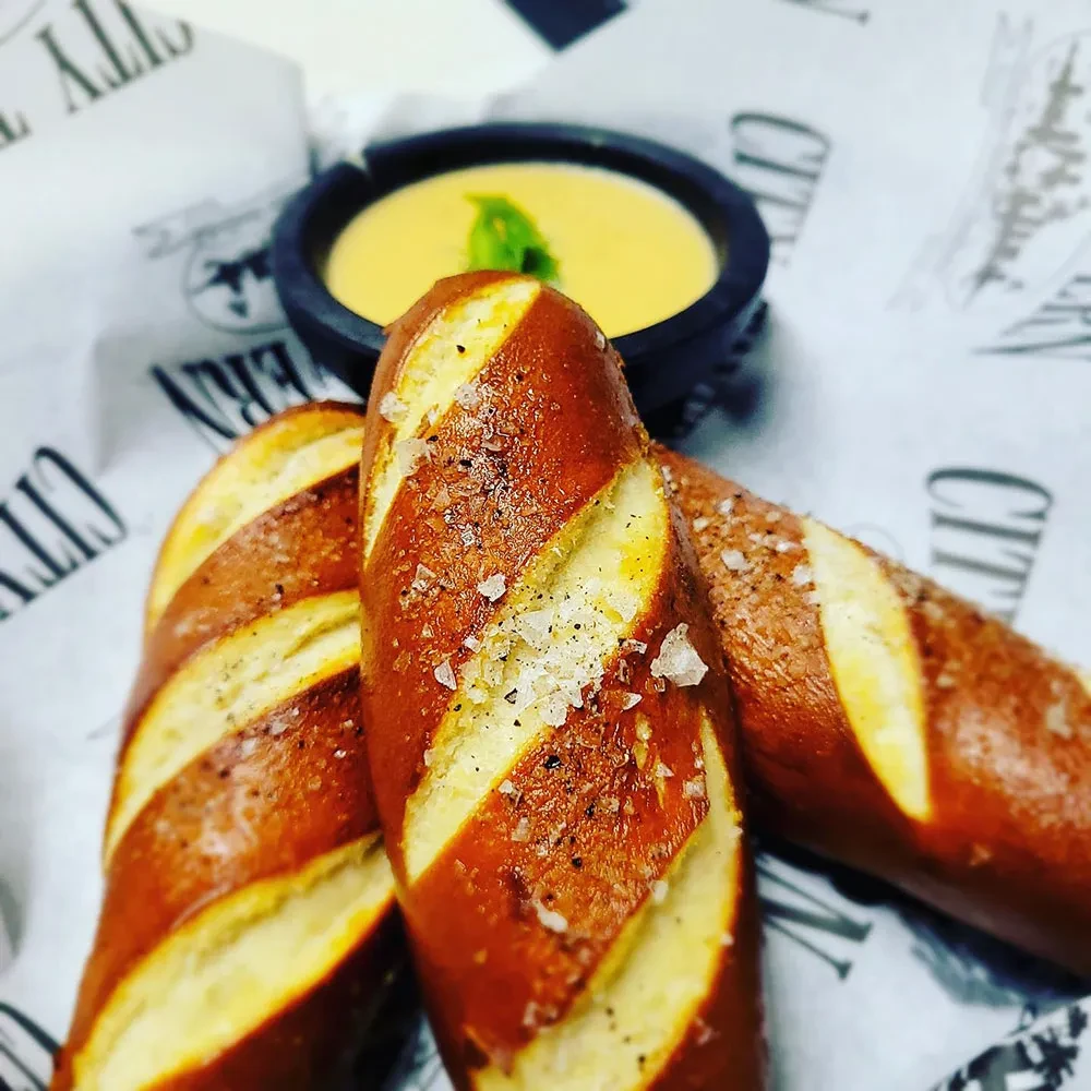 Salted, peppered pretzels with yellow dip and branded paper.
