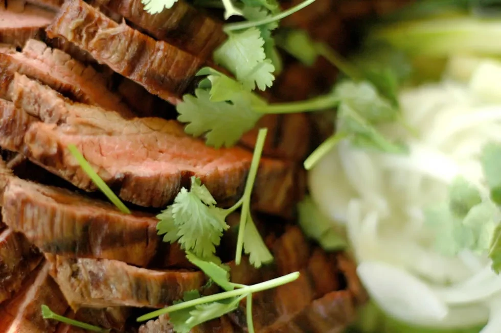 Thinly sliced medium-rare steak garnished with fresh green cilantro on a platter.