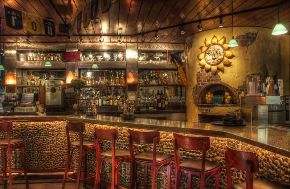 Restaurant bar interior with textured pebble counter and sun sculpture.