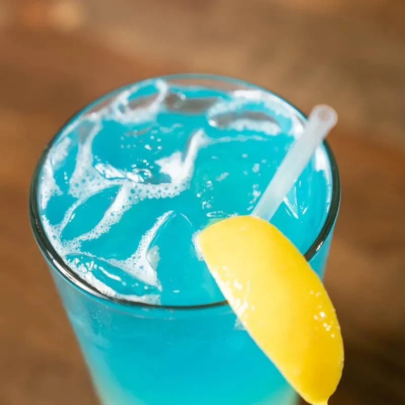Vibrant blue iced cocktail with a lemon wedge and straw.