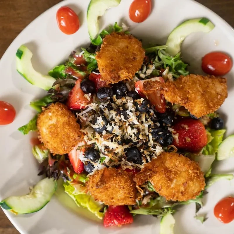 Mixed green salad with strawberries, blueberries, coconut, and fried pieces.