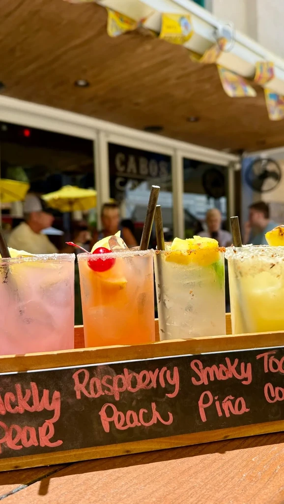 Colorful cocktail flight on a tray with names, at an outdoor bar.