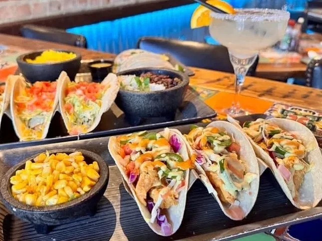 Assortment of Mexican tacos, sides, and a margarita on a restaurant table.