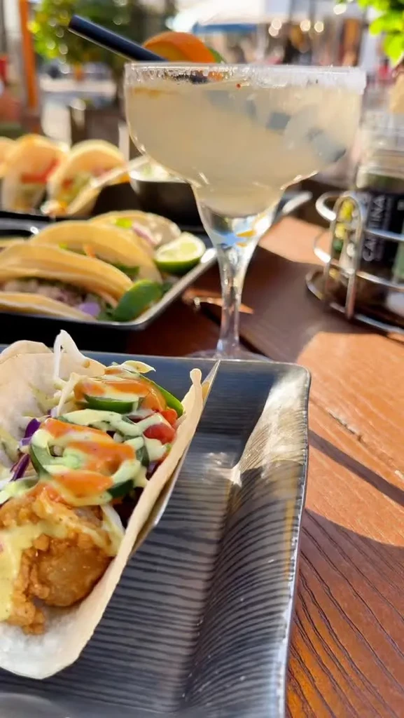 A single loaded taco and a margarita on an outdoor wooden table.