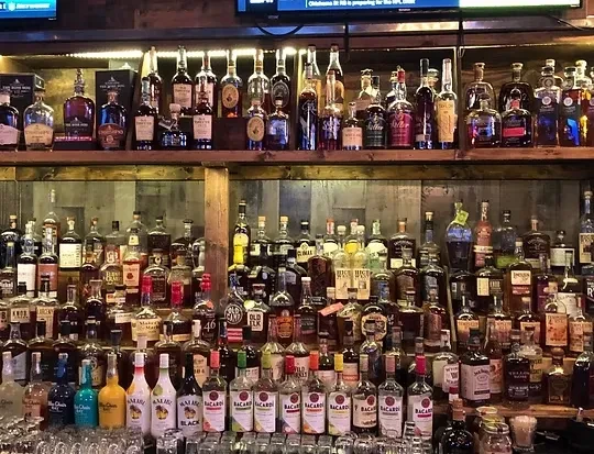 Extensive collection of liquor bottles on multiple wooden bar shelves.