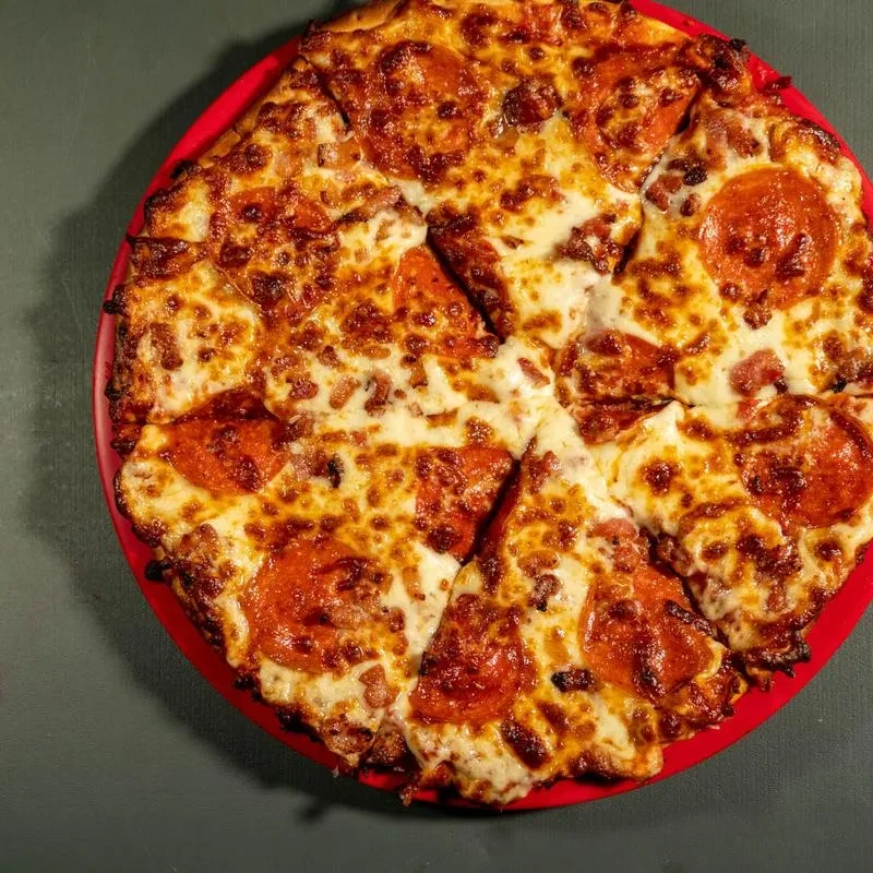 Whole pepperoni pizza, sliced, with bubbly cheese on a red plate.