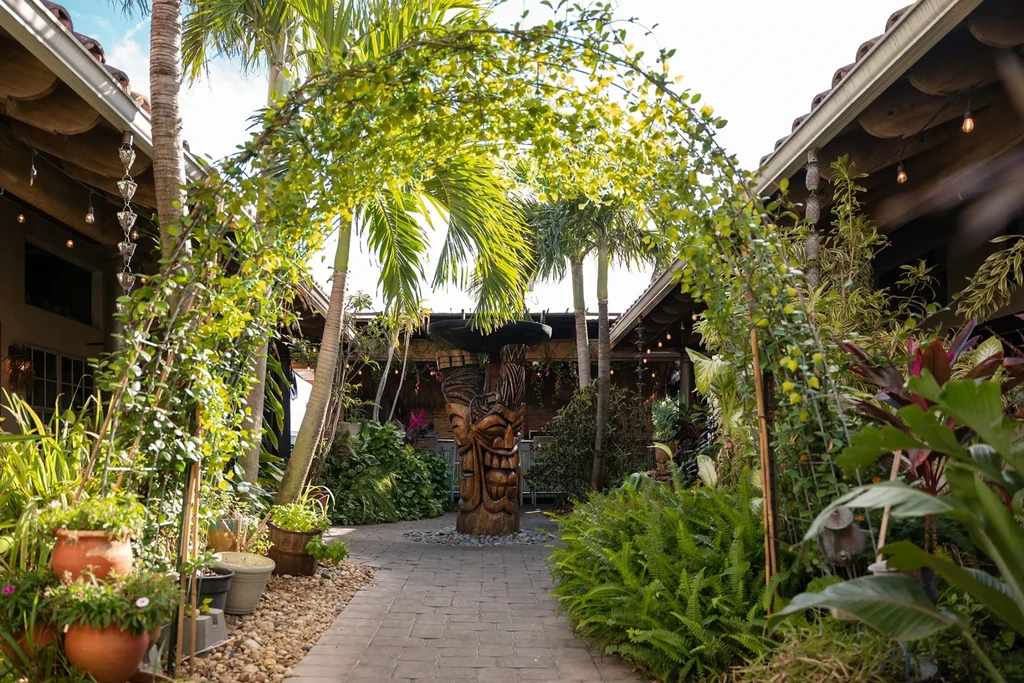 Large wooden tiki statue in a lush tropical garden courtyard.