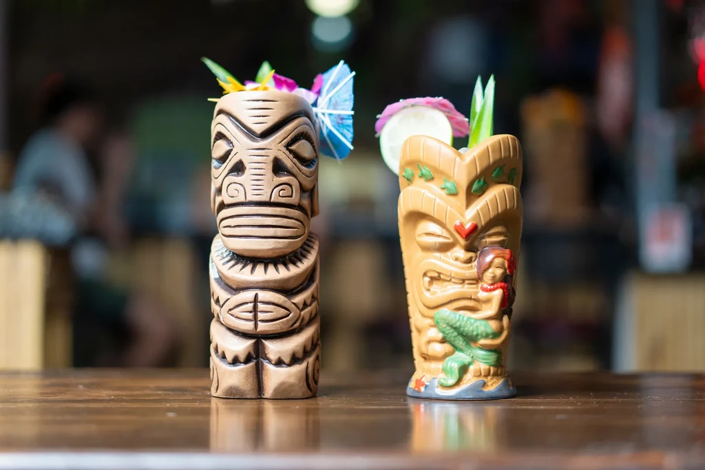 Two elaborately carved tiki mugs with drinks and colorful garnishes.