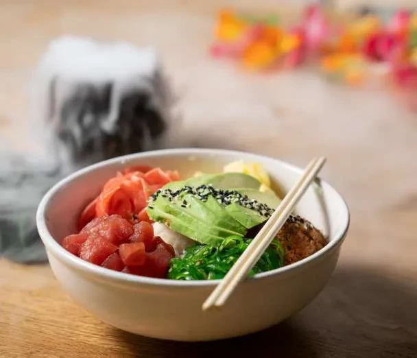 Close-up, vibrant poke bowl with tuna, avocado, seaweed, ginger, chopsticks.