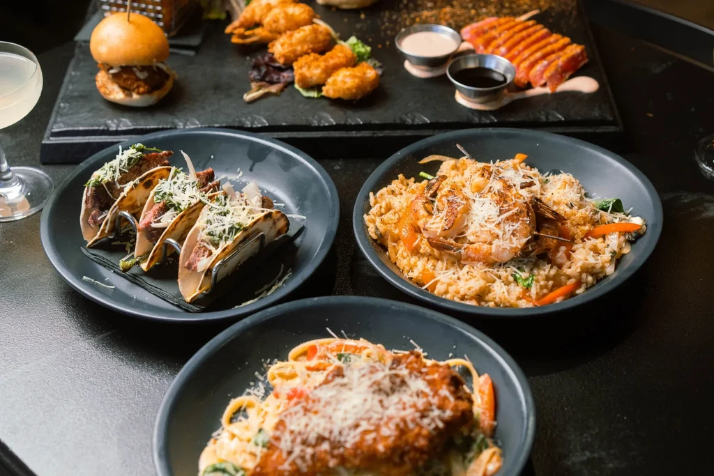 Restaurant table set with tacos, shrimp risotto, pasta, tuna, and fried food.