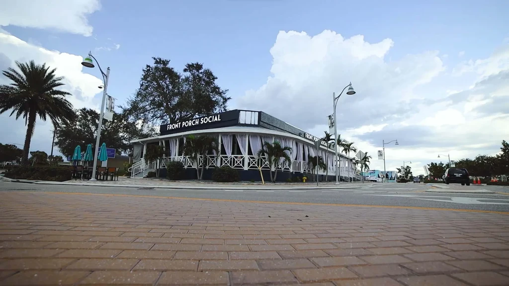 Front Porch Social restaurant exterior with rounded corner, outdoor seating, and palms.