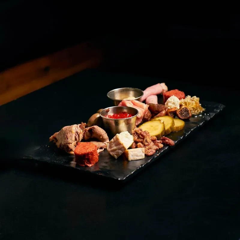 Dark charcuterie board with meats, cheeses, nuts, honeycomb, and sauces.