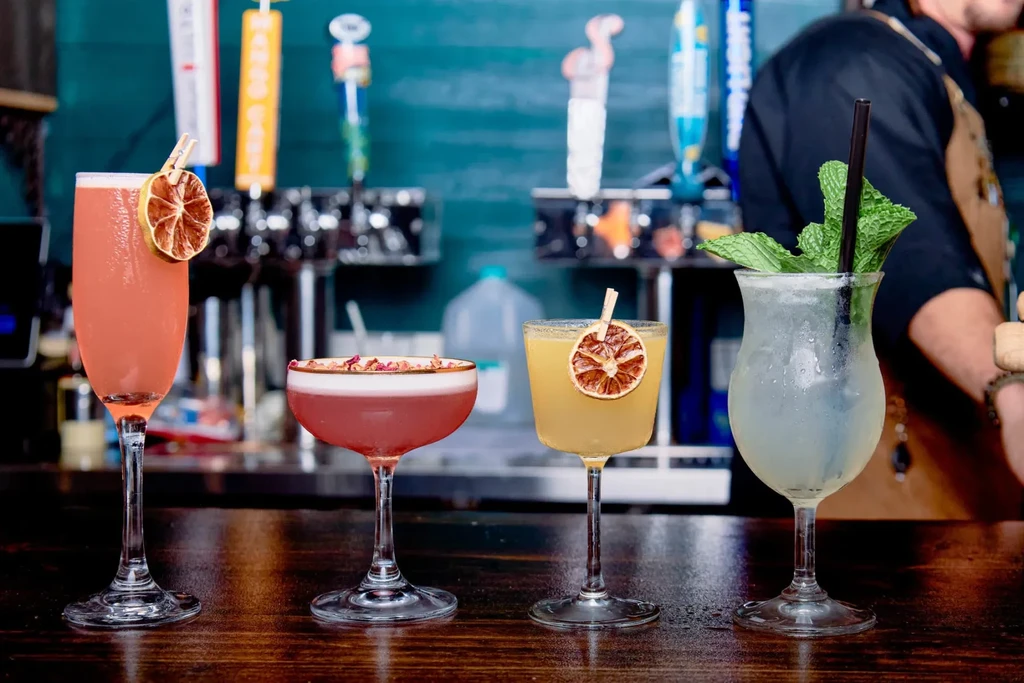 Four distinct cocktails on a bar counter with various garnishes.
