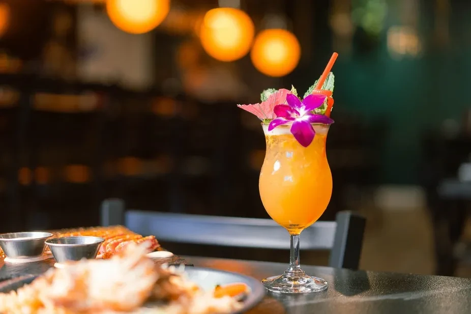 Vibrant orange cocktail in a hurricane glass with orchid and umbrella.