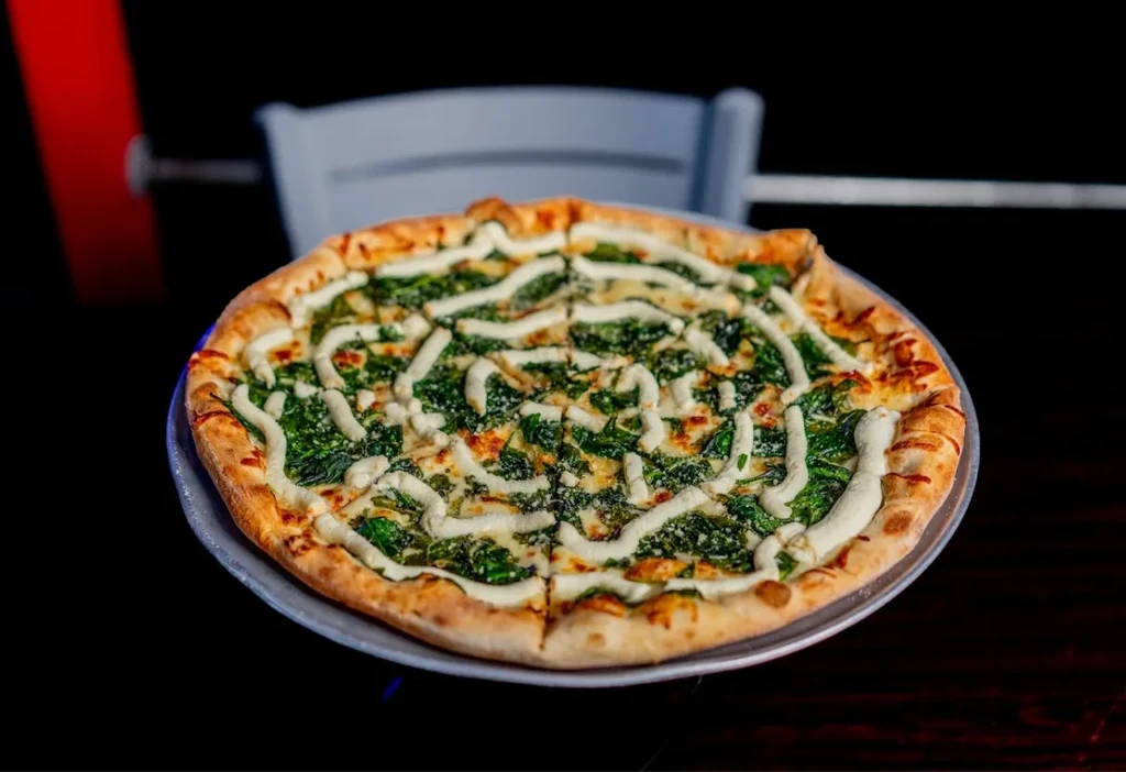 Spinach and cheese pizza with white drizzle, sliced on a metallic pan.