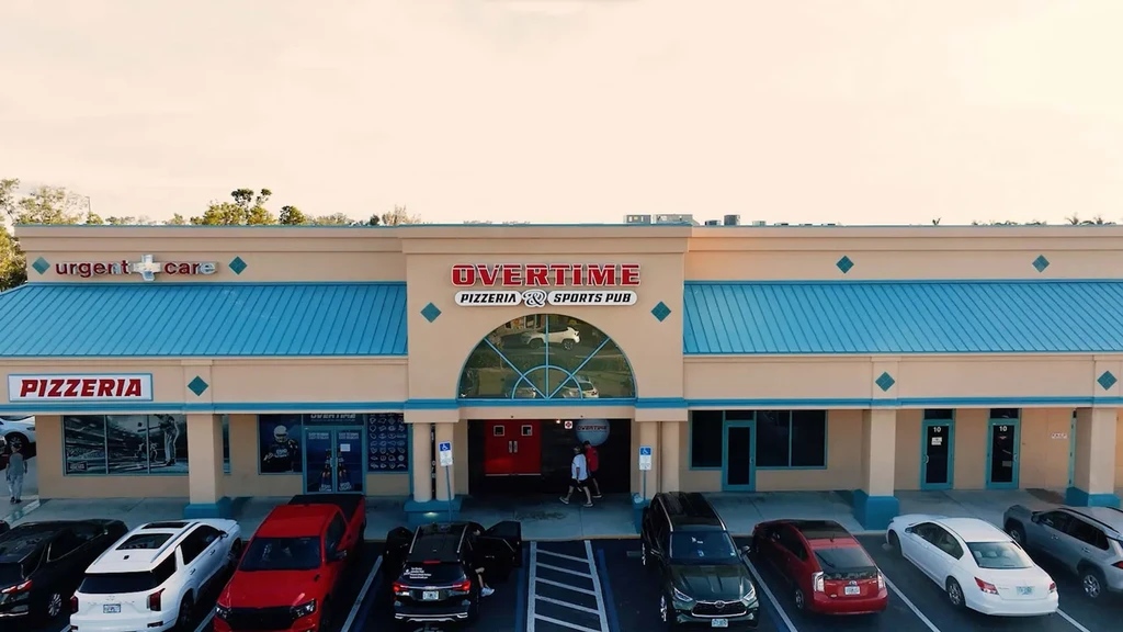 Daytime aerial view of a strip mall featuring Overtime Pizzeria.