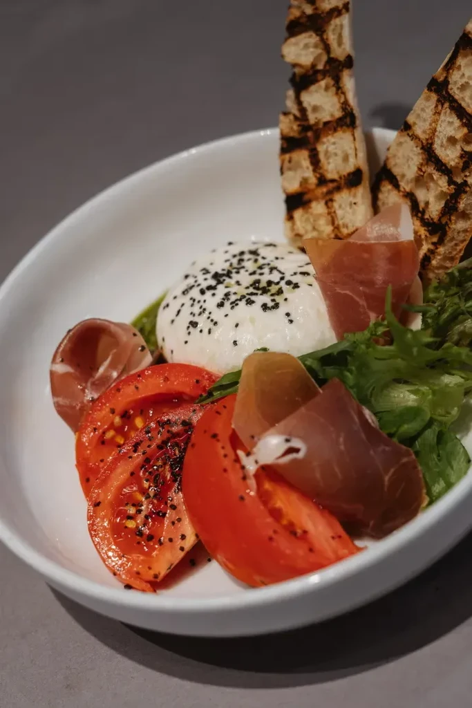 Appetizer of burrata, tomatoes, prosciutto, pesto, and grilled bread.