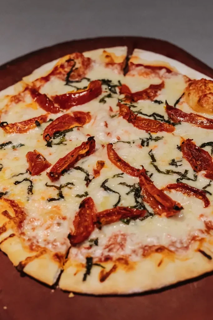 Sliced pizza with melted mozzarella, sun-dried tomatoes, and fresh basil.