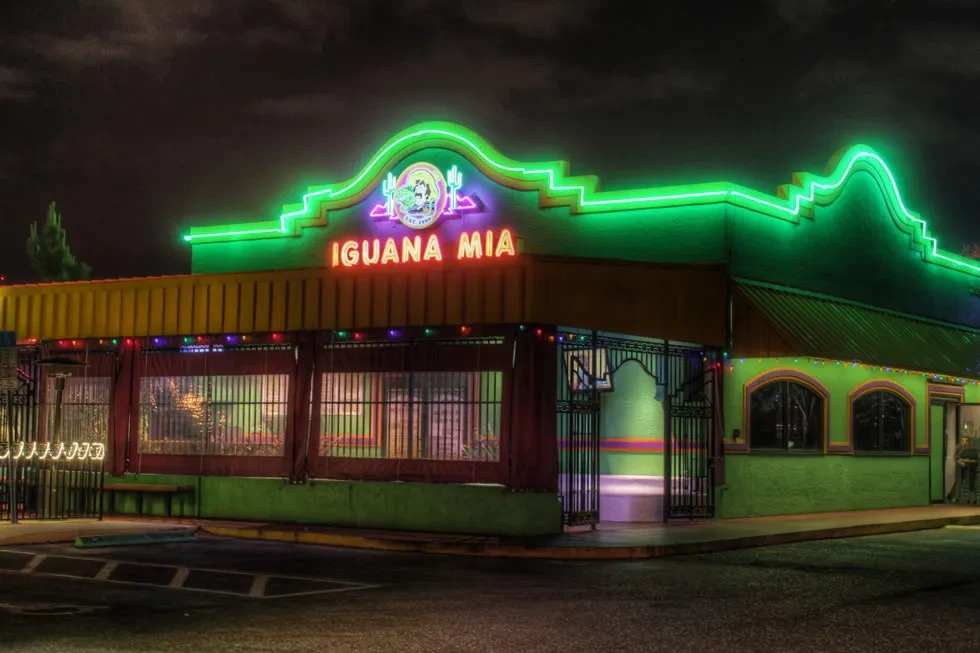 Iguana Mia restaurant exterior at night with green neon and wavy roof.