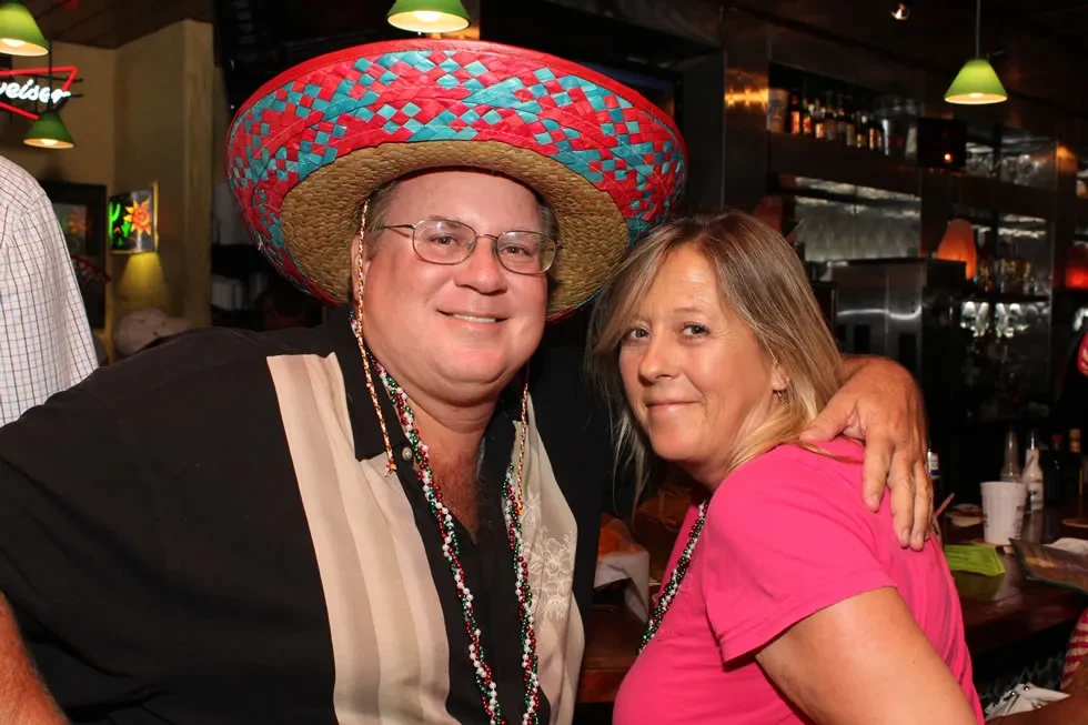 Smiling man in sombrero and woman in pink shirt at a bar.