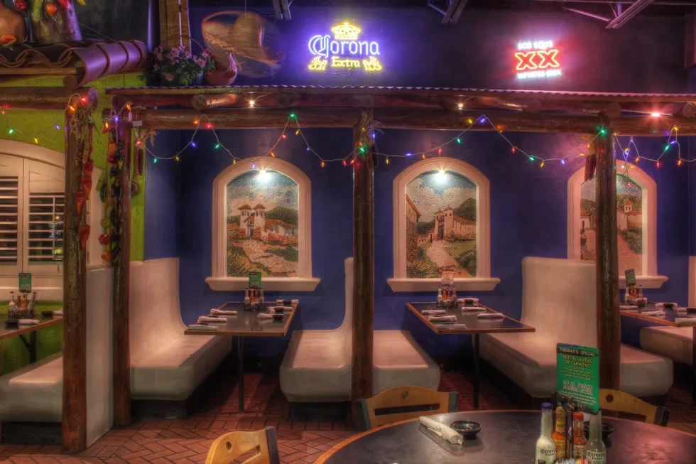Festive Mexican restaurant interior with blue/green walls, booths, and neon signs.