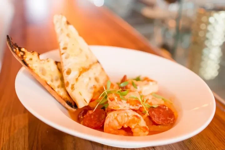 Shrimp and chorizo in orange sauce with bread and green herbs.