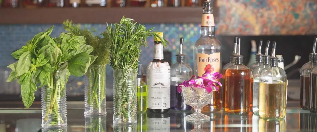 Bar counter with fresh herbs, spirits, mixers, and purple orchid garnish.
