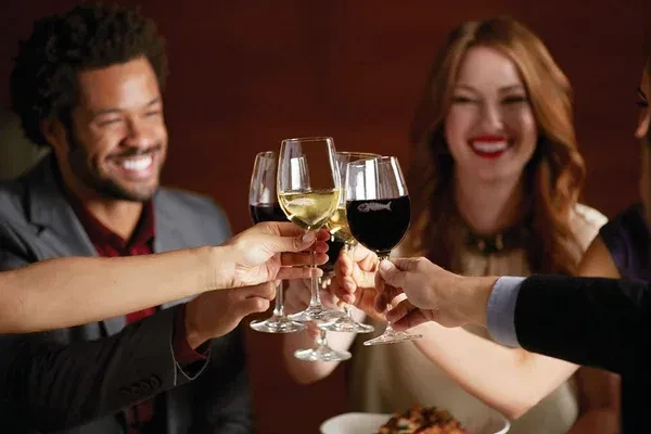 Four wine glasses clinking, two red and two white, with smiling faces.