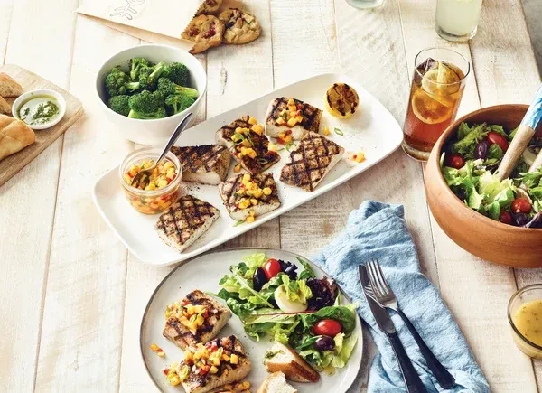 A table spread with grilled fish, fruit salsa, salads, and vegetables.