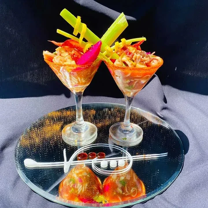 Two vibrantly garnished seafood cocktails in martini glasses on a dark tray.