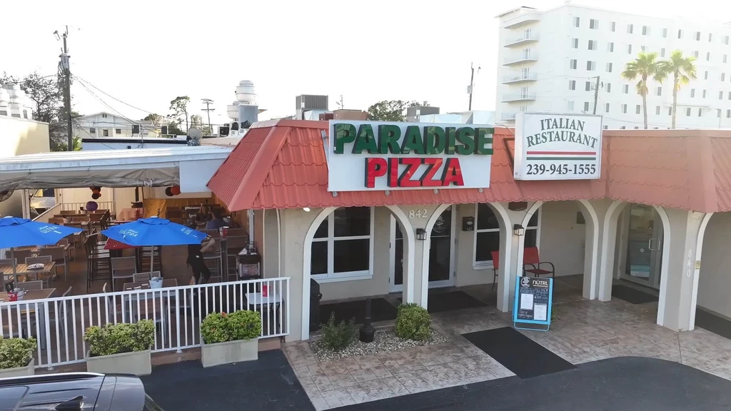 Paradise Pizza Italian restaurant exterior with bustling patio and palm trees.