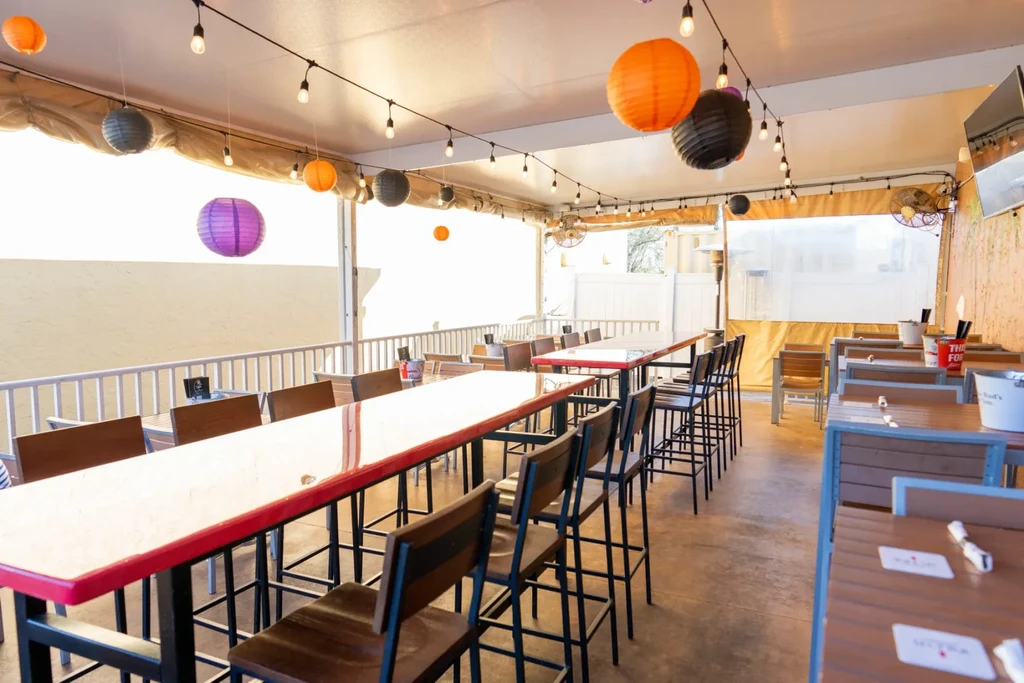 Brightly lit, empty restaurant patio with tables, chairs, and colorful lanterns.
