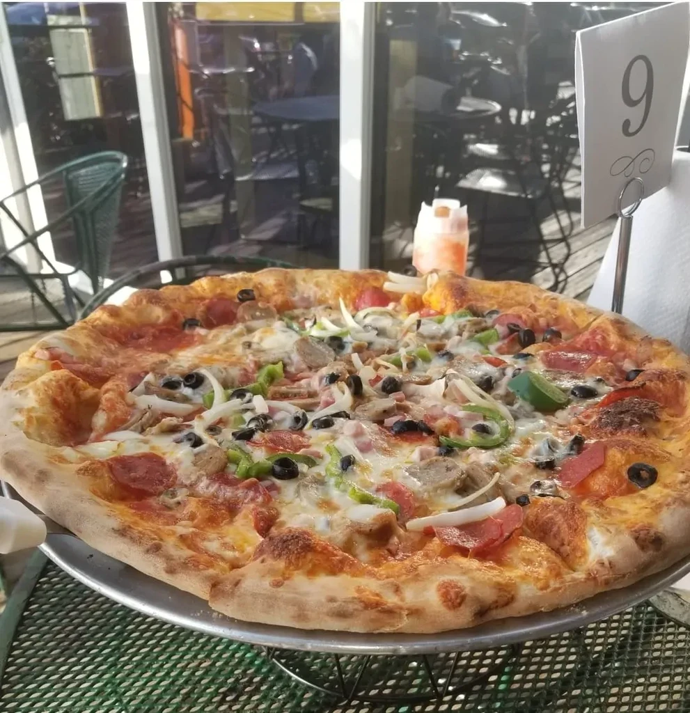 Large pizza with pepperoni, olives, and cheese on an outdoor table.