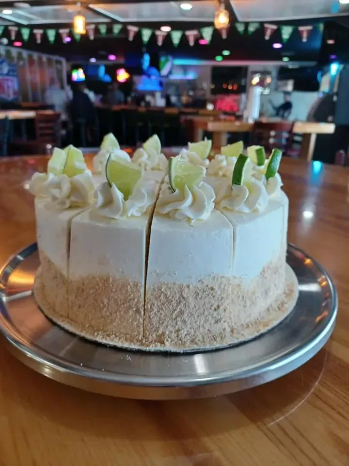 Pre-sliced creamy lime pie with whipped cream, lime garnish, on a platter.