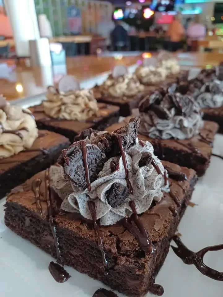 Close-up of brownies with varied frosting, cookie pieces, and chocolate drizzle.