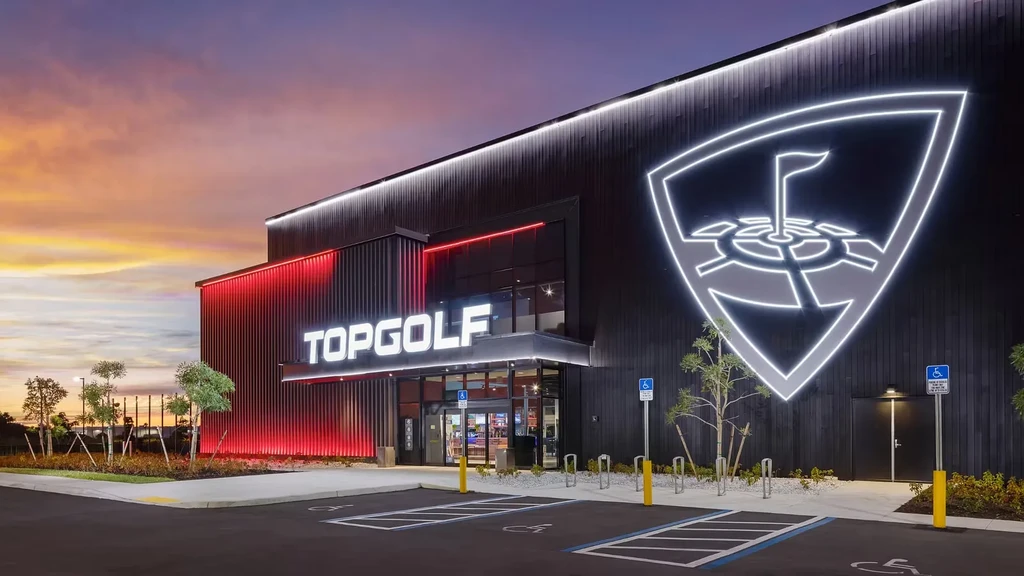 Modern TOPGOLF building illuminated by neon lights at dusk.