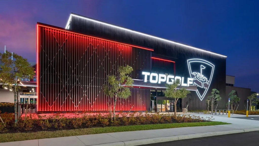 Illuminated Topgolf building exterior at dusk with red and white lights.