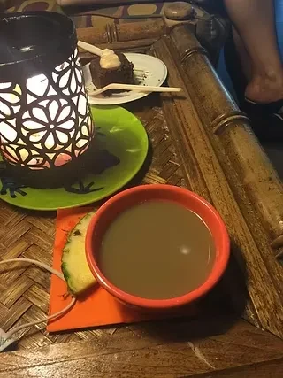 Orange drink, chocolate cake, pineapple, lit lantern on bamboo table.