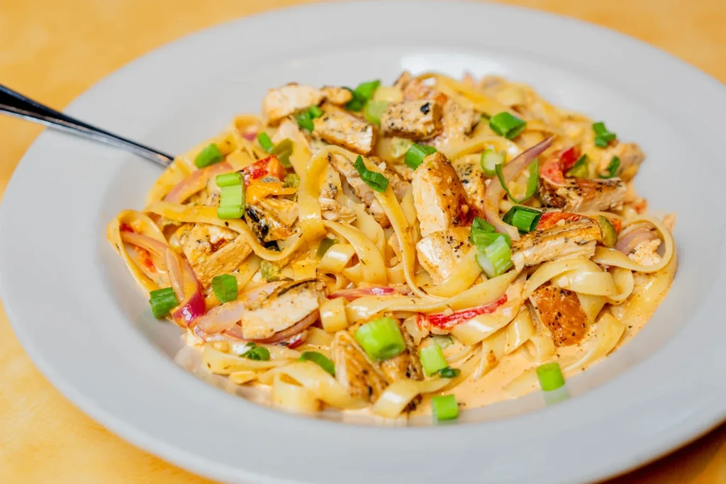 Creamy fettuccine pasta with grilled chicken, red bell peppers, and onions.