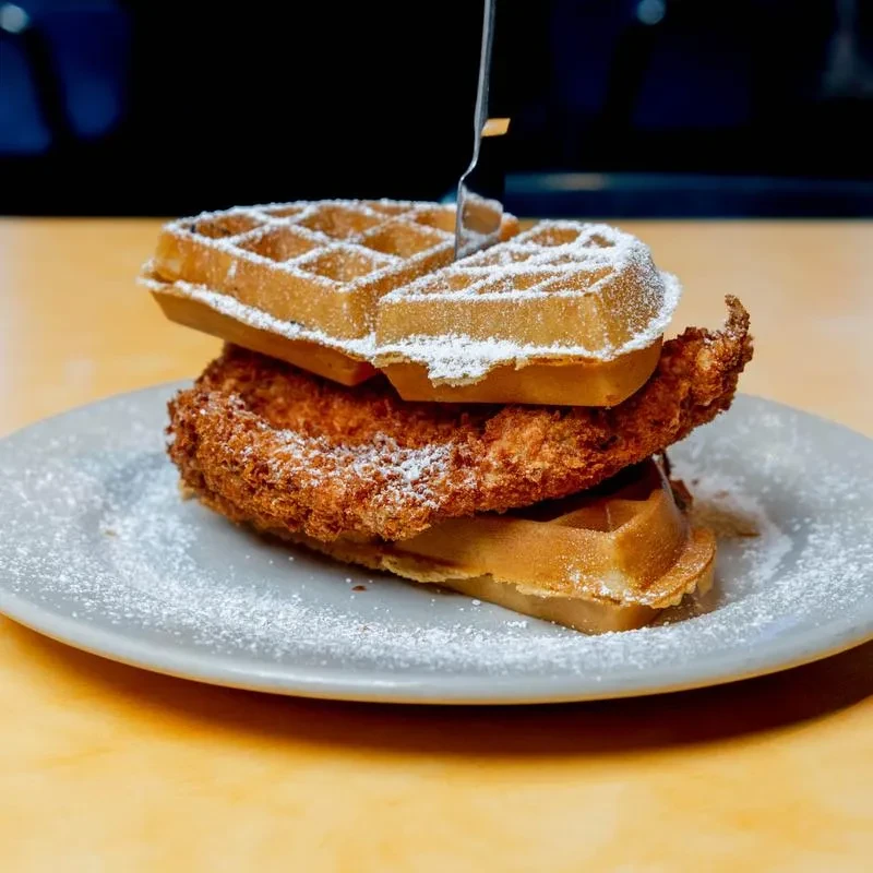 Skewered crispy chicken and waffles stack with powdered sugar.