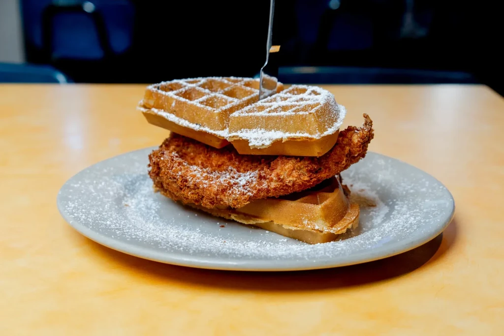 Close-up of chicken and waffles stacked, dusted with powdered sugar.