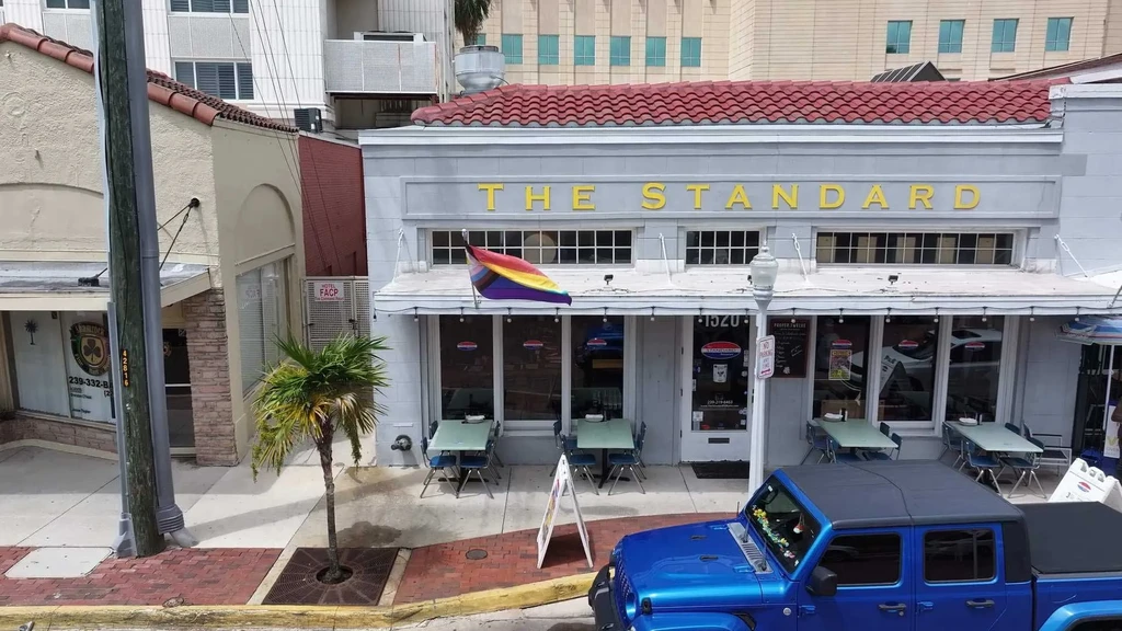 Street view of THE STANDARD building, outdoor tables, progress flag.