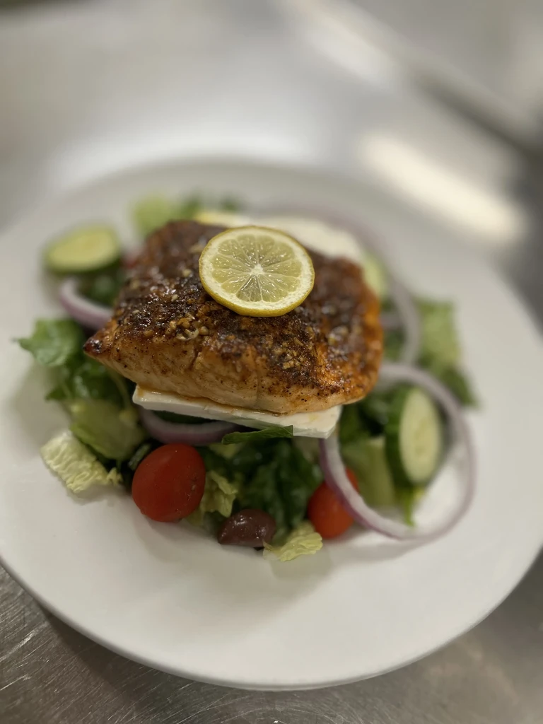 Seasoned salmon fillet on green salad with lemon and feta cheese.