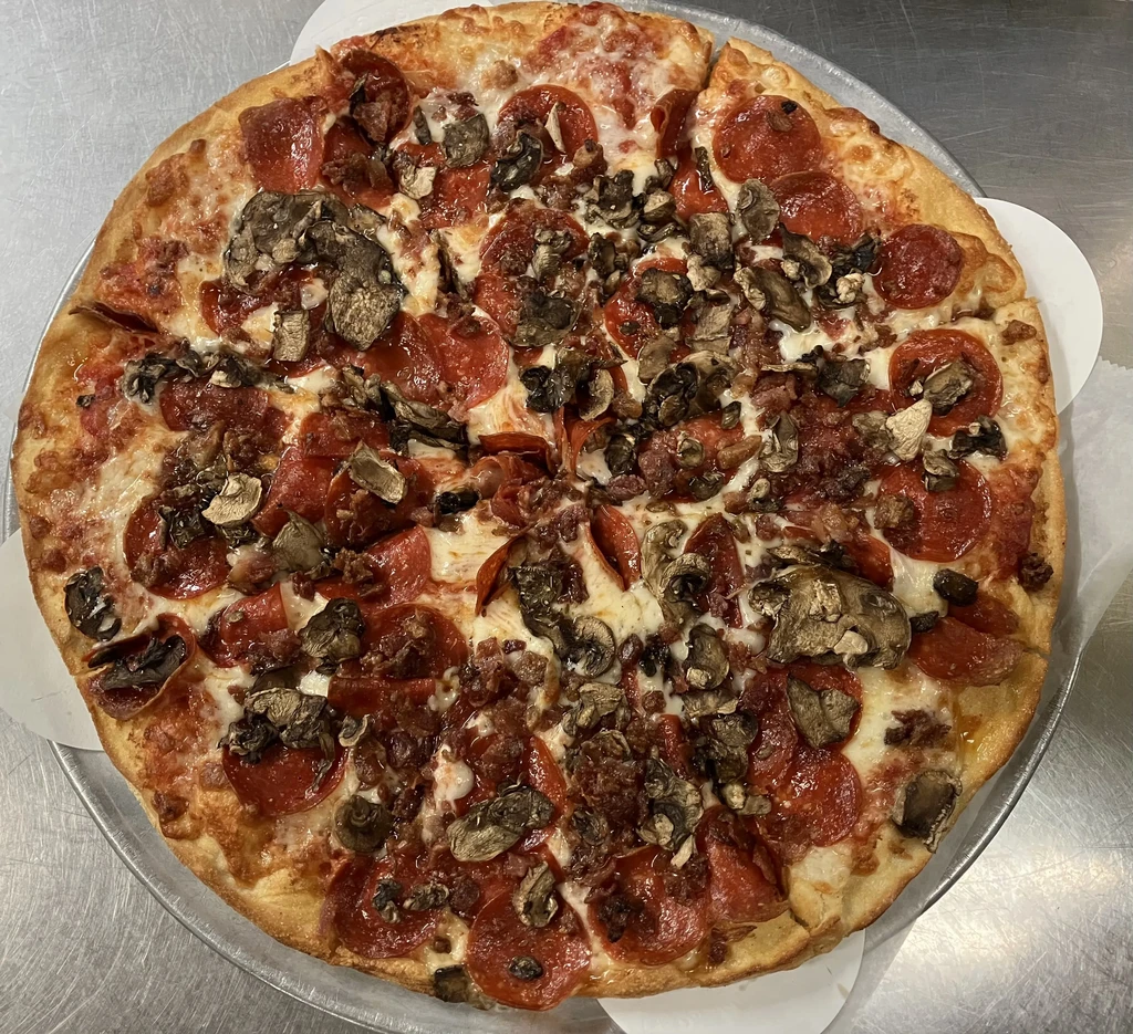 Whole pizza with pepperoni, mushrooms, and crumbled meat on pan.