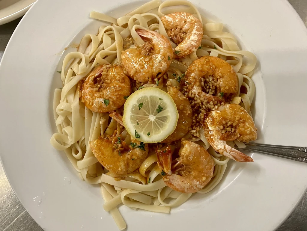 Overhead fettuccine pasta with peeled shrimp, orange sauce, lemon, and fork.