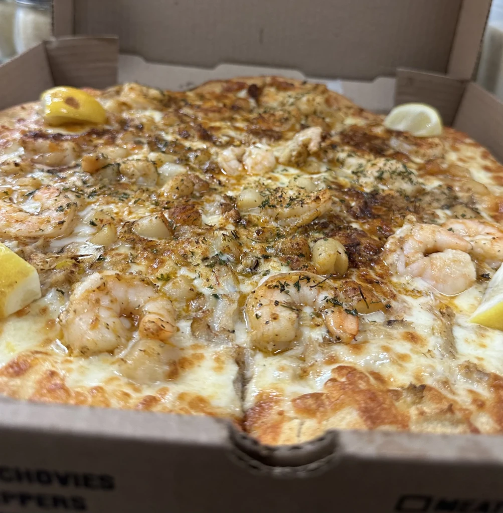 Shrimp and scallop pizza with lemon wedges in a takeout box.