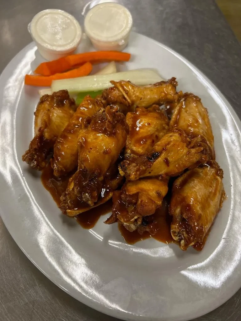 Plate of glossy, sauced chicken wings with carrot, celery, and dipping sauces.