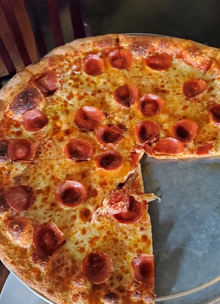Round pepperoni pizza on metal pan, melted cheese, curled pepperoni, one slice missing.
