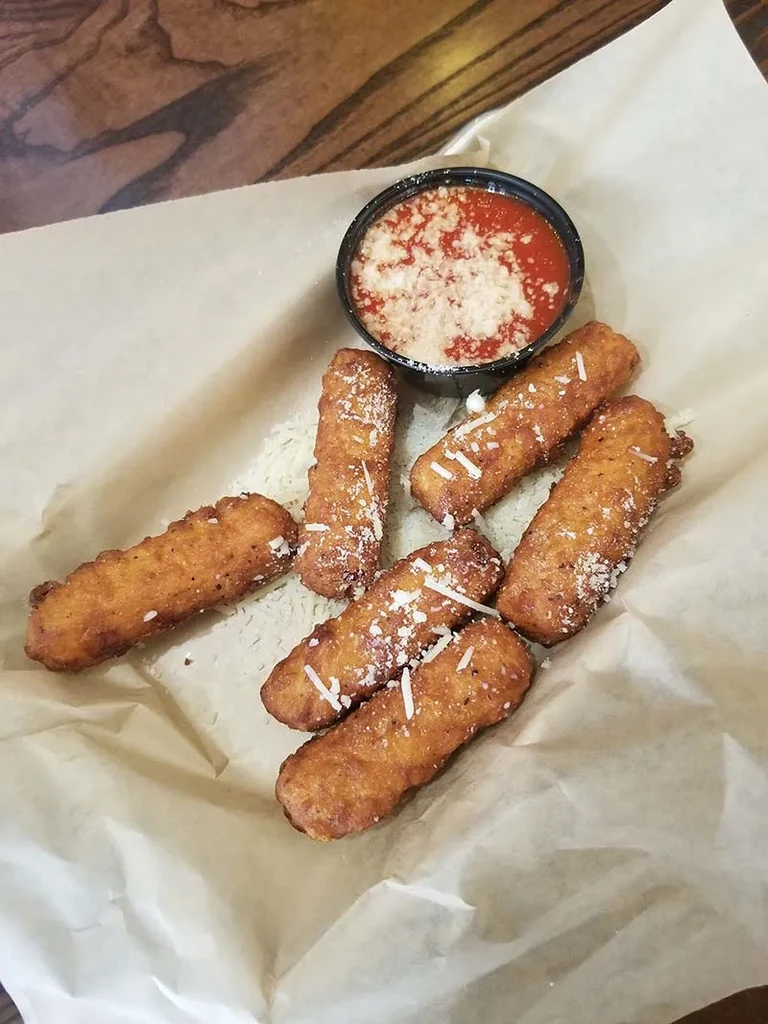 Seven fried mozzarella sticks with marinara sauce and grated cheese.