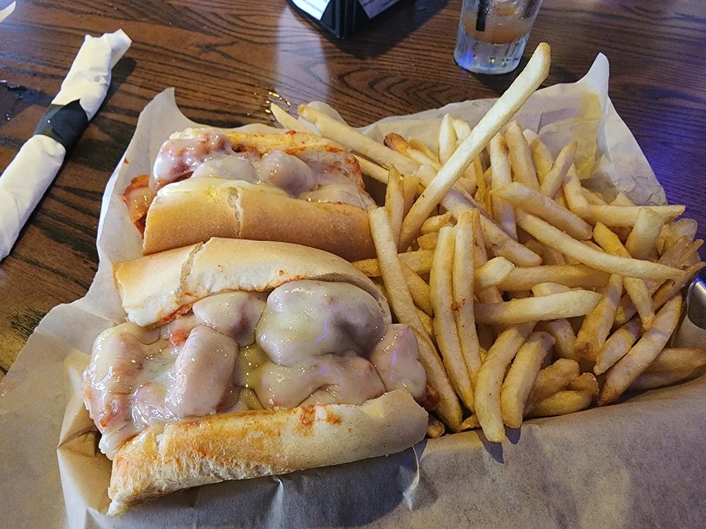 Meatball sub sandwich with melted cheese and golden fries in a basket.